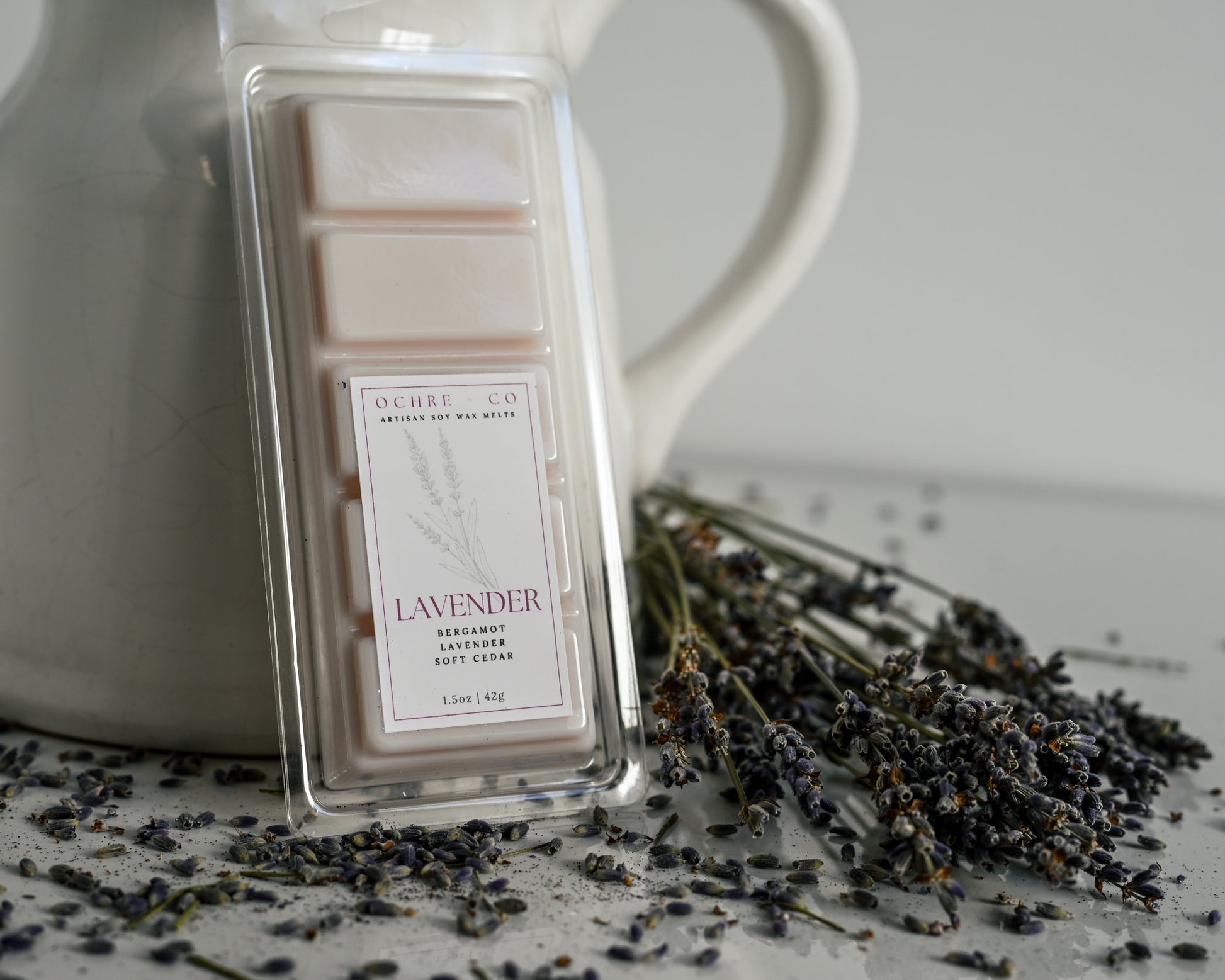 Ochre & Co lavender wax melt with a white pitcher and lavender flowers on a light background