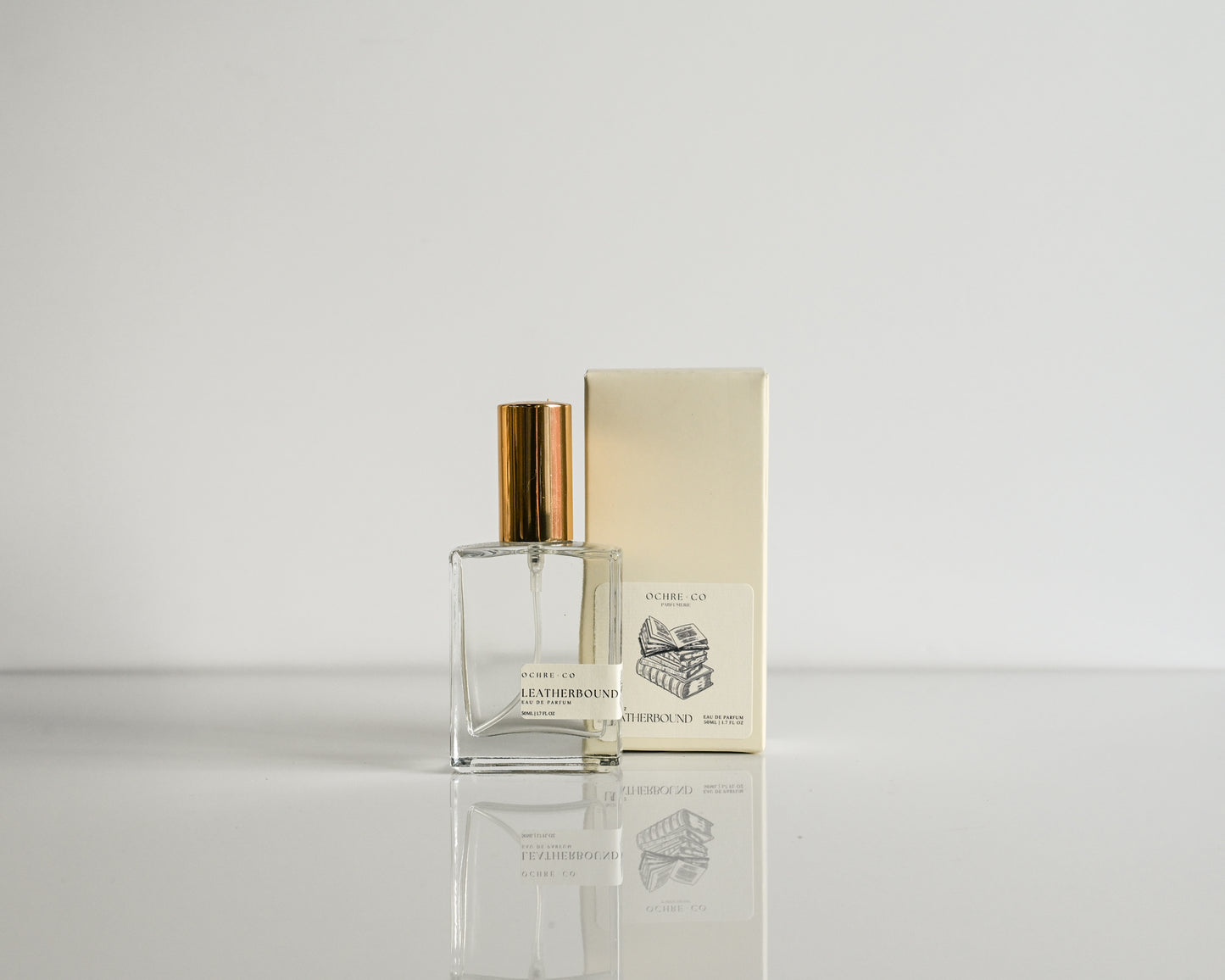 Perfume bottle with gold cap and packaging on a light gray background