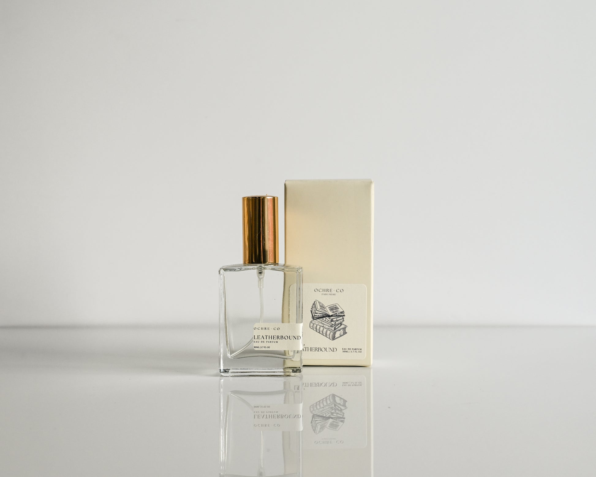 Perfume bottle with gold cap and packaging on a light gray background