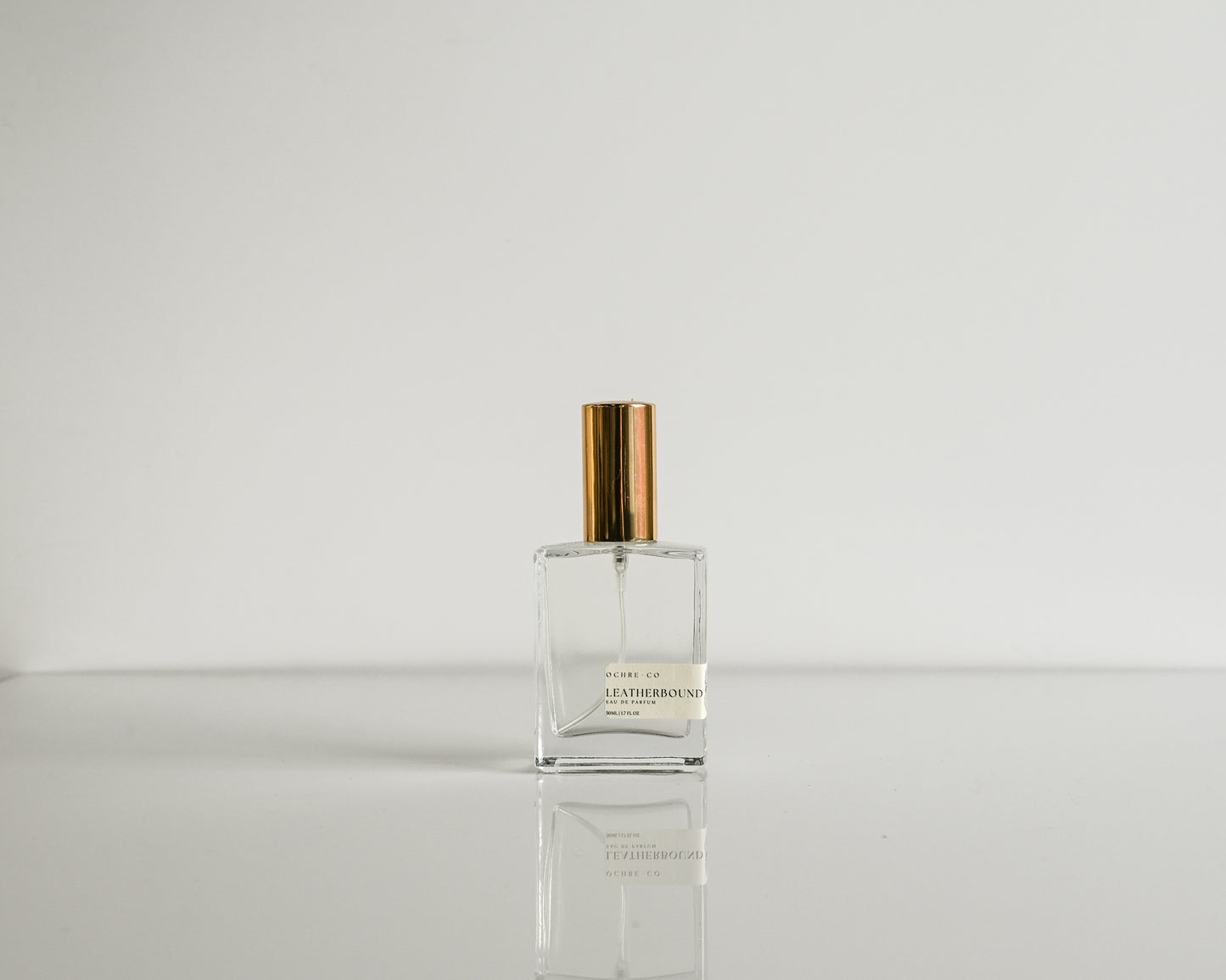 Perfume bottle with gold cap on a reflective surface and light gray background