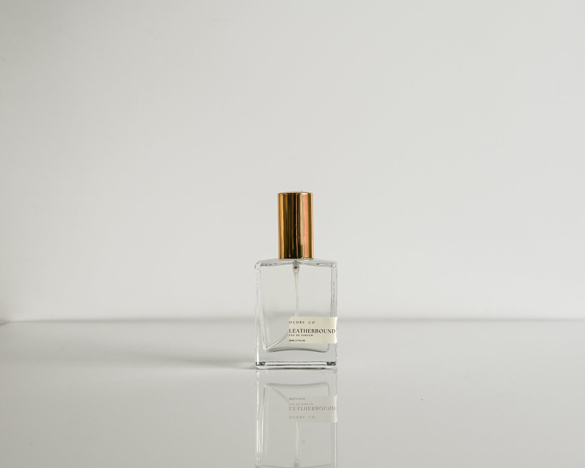 Perfume bottle with gold cap on a reflective surface and light gray background