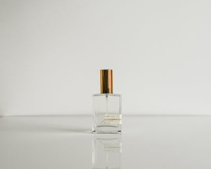 Perfume bottle with gold cap on a reflective surface and light gray background