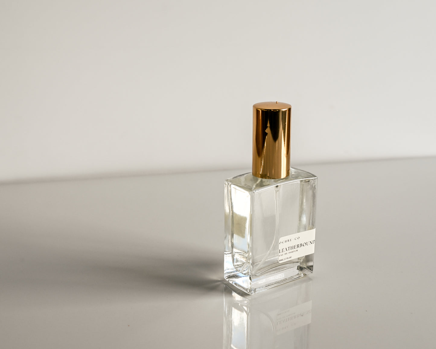 Clear perfume bottle with gold cap on a reflective surface