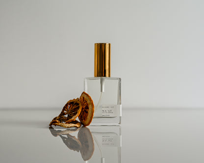 Perfume bottle of Ma'at with gold cap and dried lemon slices on a reflective surface