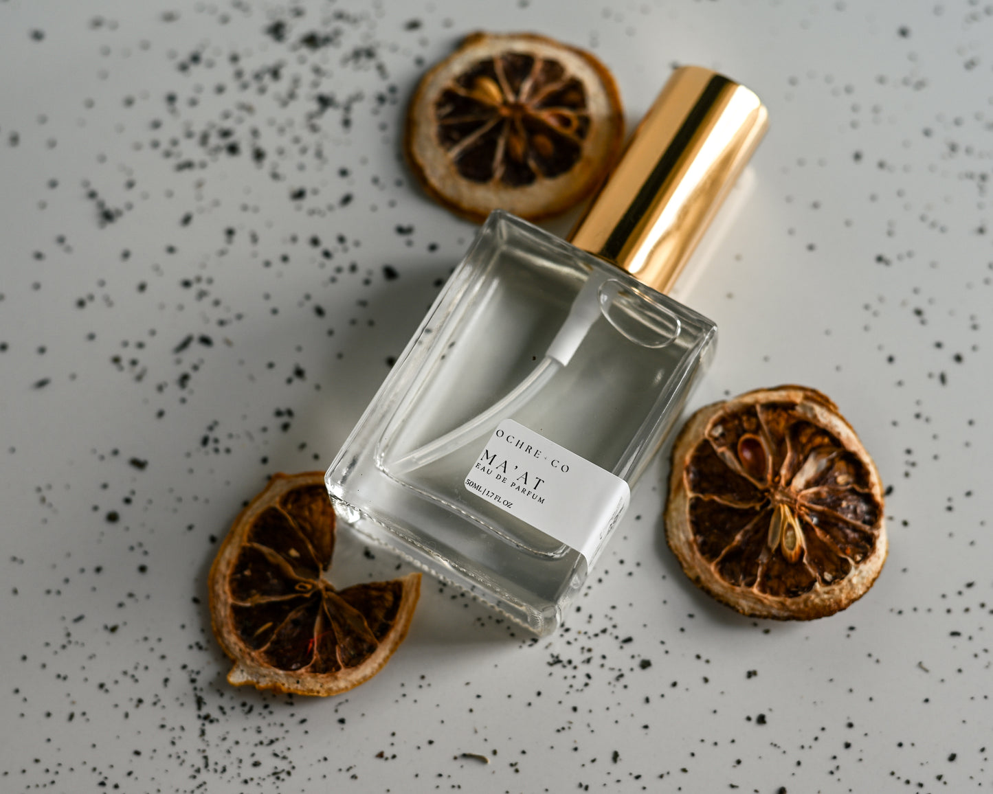 Perfume bottle of Ma'at with gold cap and dried lemons on a speckled surface