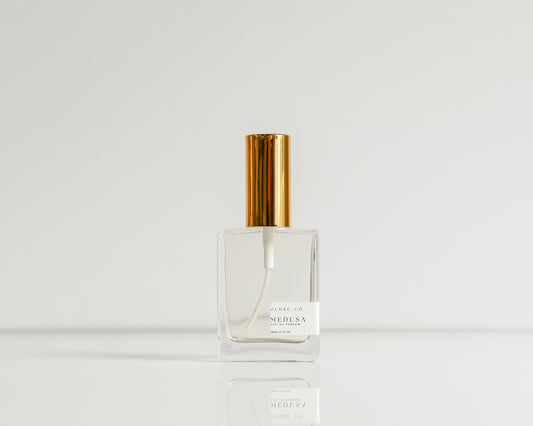 A clear glass perfume bottle with gold cap on white background, named "MEDUSA"