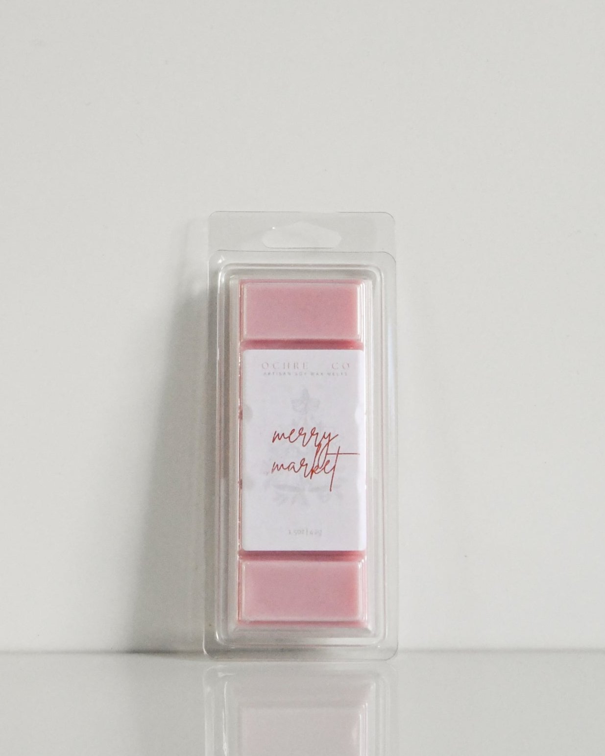 A soft red wax melt in its packaging, leaning on a wall, on a white background, label reading "Merry Market"