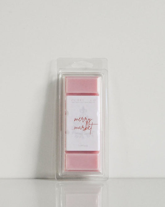 A soft red wax melt in its packaging, leaning on a wall, on a white background, label reading "Merry Market"
