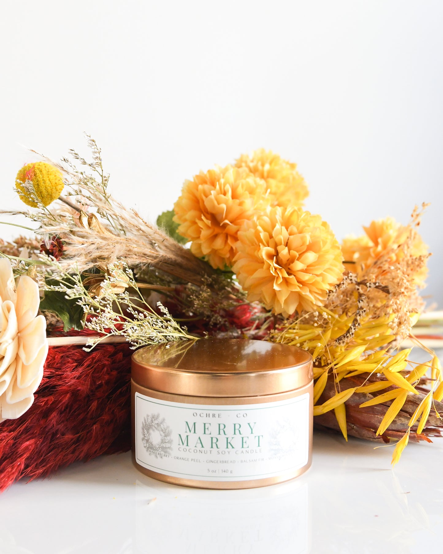A copper metal candle vessel with fall-colored florals on a white background, label reads "Merry Market"