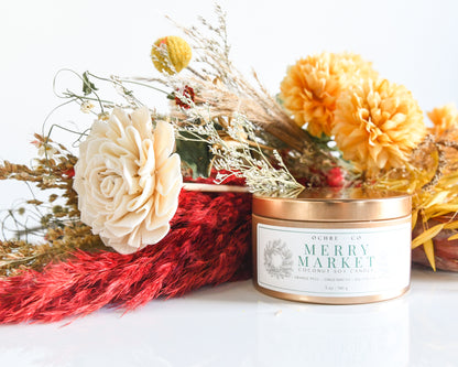 A copper metal candle vessel with fall-colored florals on a white background, label reads "Merry Market"