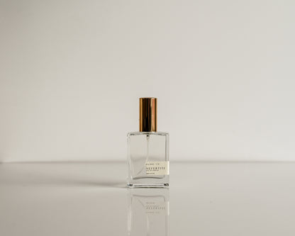 Clear perfume bottle with gold cap on a reflective surface and light gray background