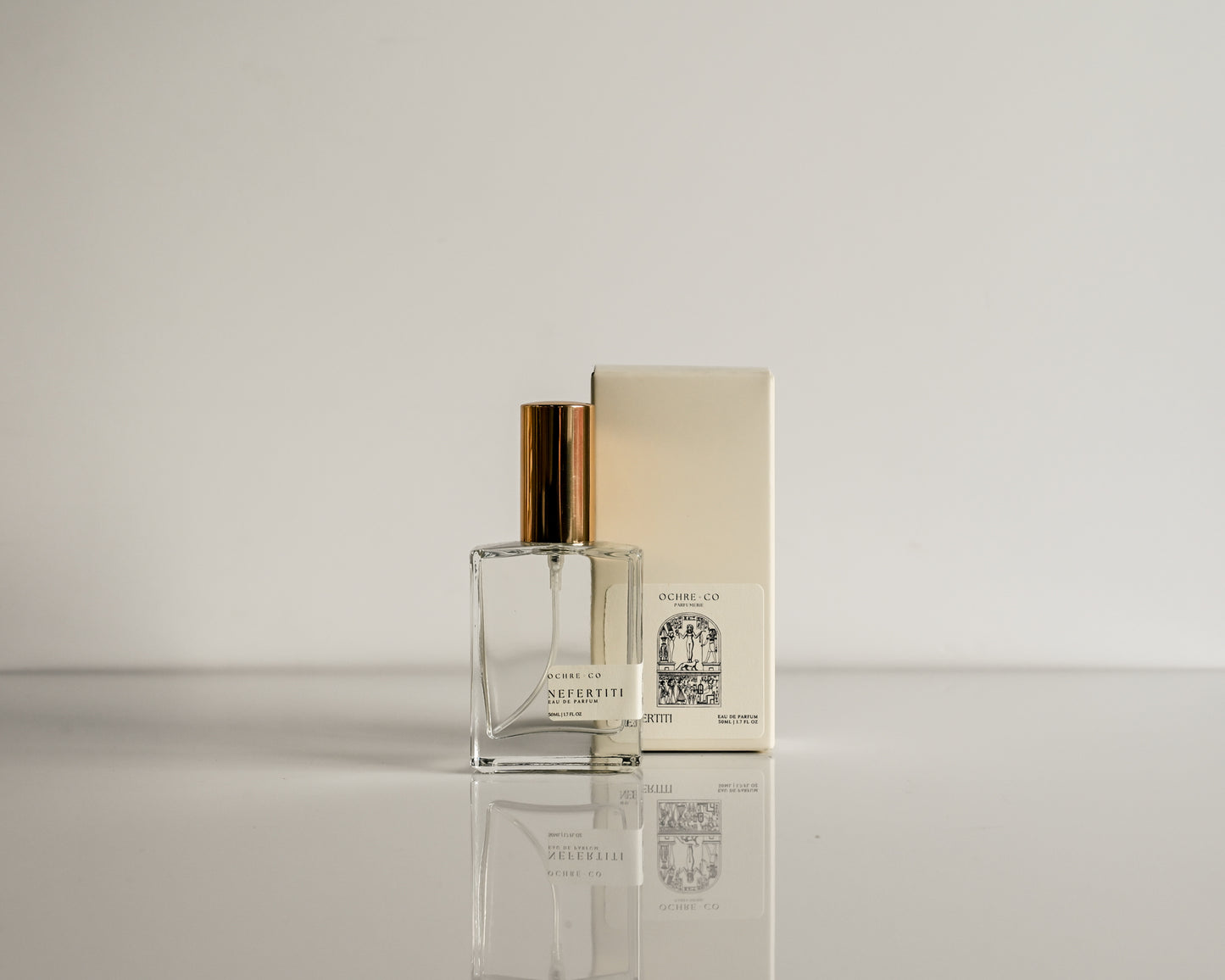 Perfume bottle with gold cap and packaging on a reflective surface
