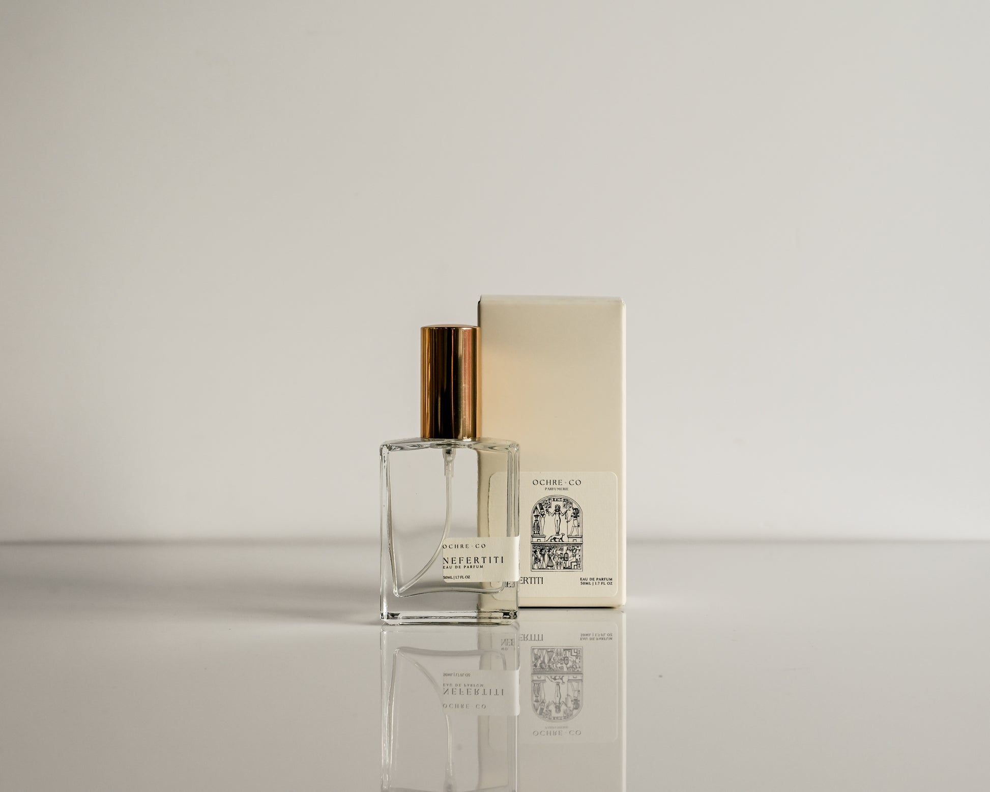 Perfume bottle with gold cap and packaging on a reflective surface