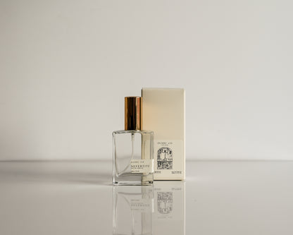 Perfume bottle with gold cap and packaging on a reflective surface