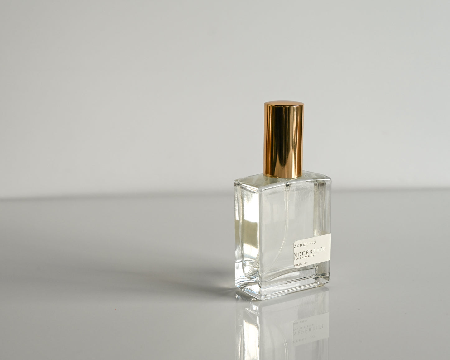 Clear perfume bottle with gold cap on a gray background