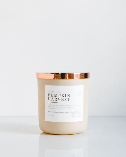 A matte beige coconut soy candle with a copper lid, labeled 'PUMPKIN HARVEST'.