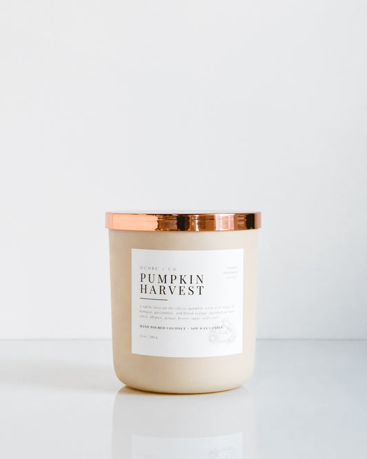 A matte beige coconut soy candle with a copper lid, labeled 'PUMPKIN HARVEST'.