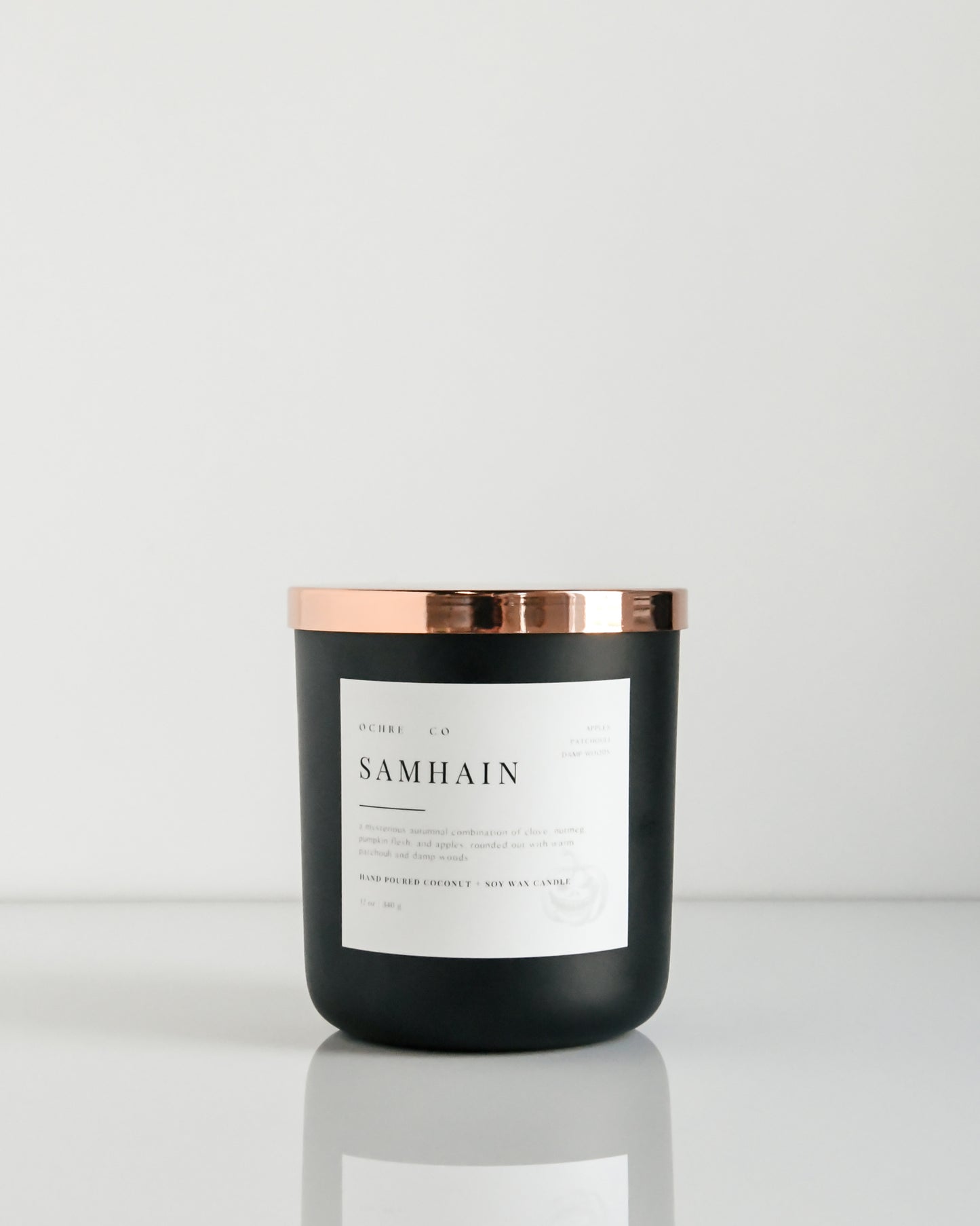 A matte black candle with a copper lid labeled 'Samhain' set against a white background.