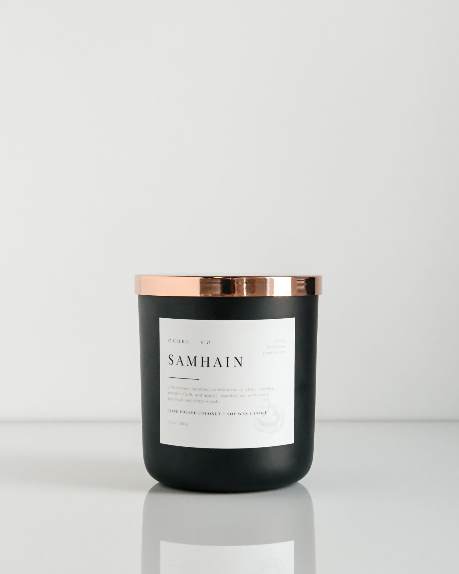 A matte black candle with a copper lid labeled 'Samhain' set against a white background.