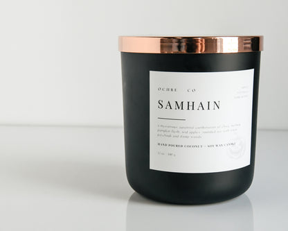 A matte black candle with a copper lid labeled 'Samhain' set against a white background.