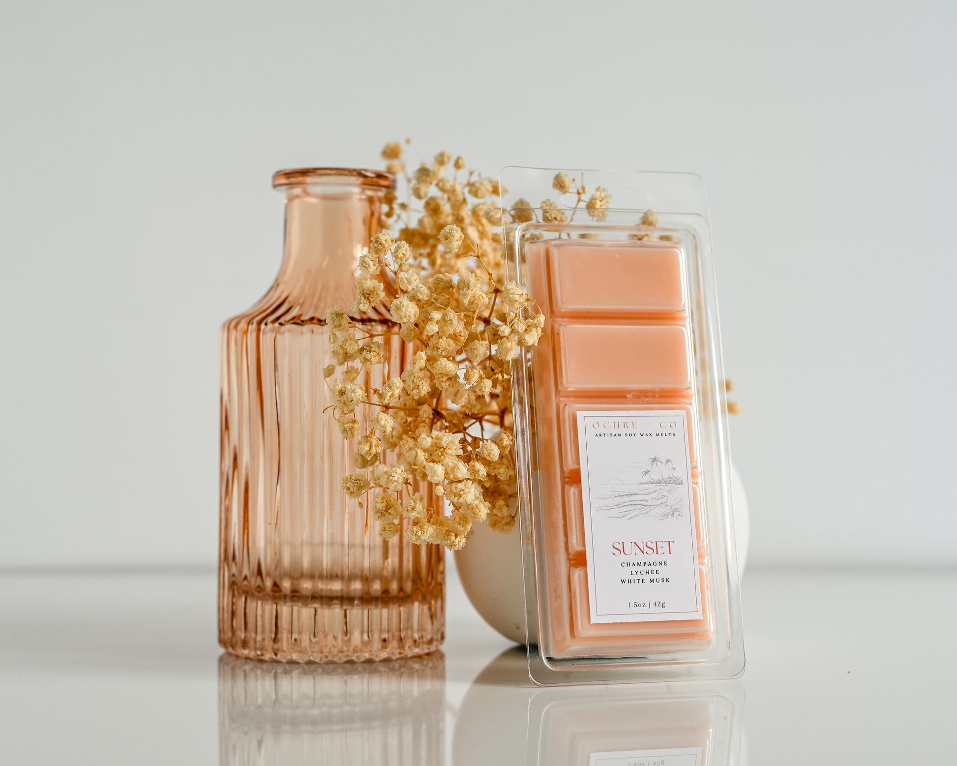 Wax melt with 'Sunset' packaging and a decorative vase on a reflective surface.