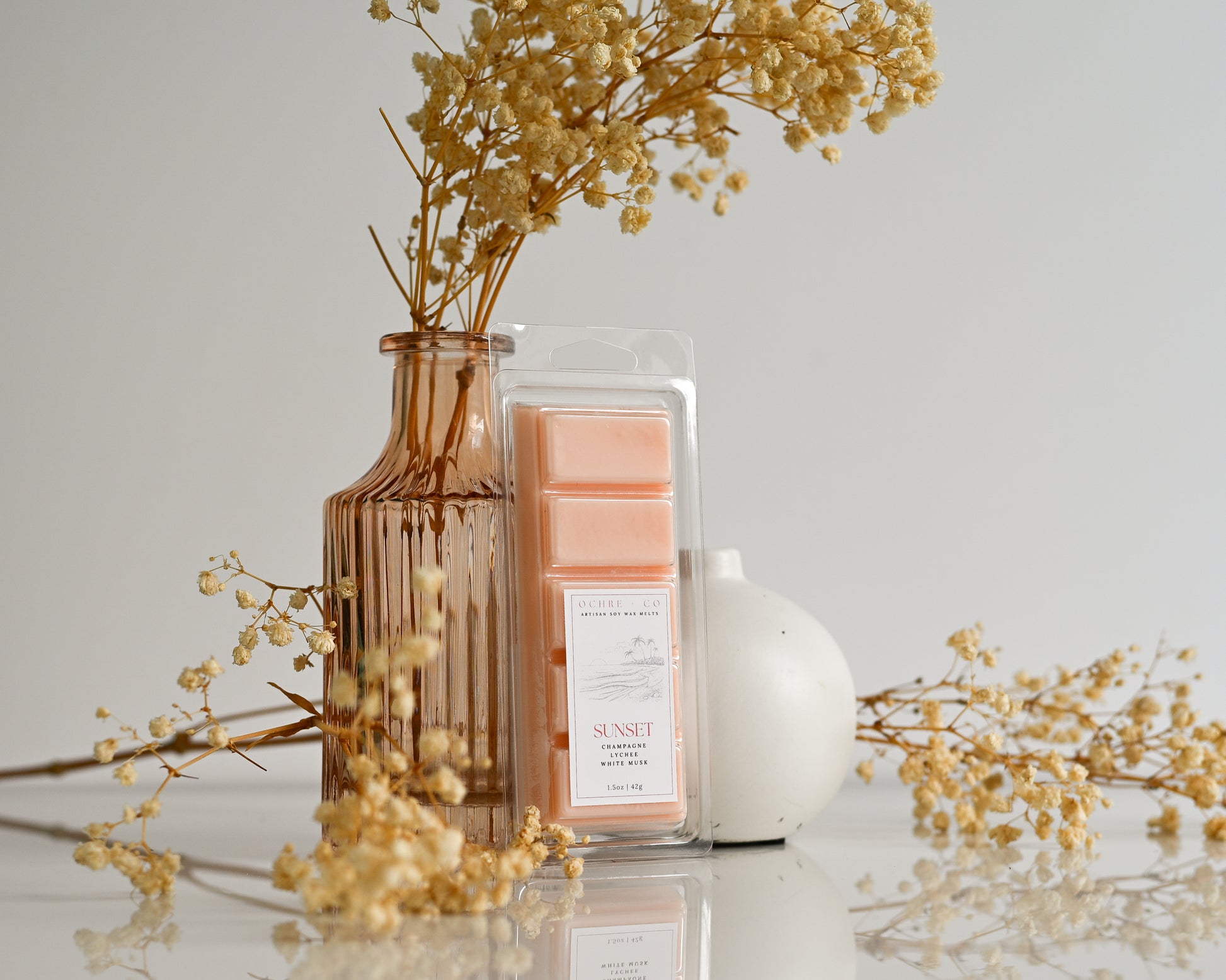 Sunset wax melts with a vase of dried flowers on a light surface.
