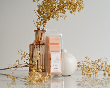 Sunset wax melts with a vase of dried flowers on a light surface.