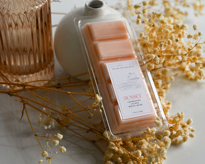 Packaged wax melts with a 'Sunset' label on a decorative surface with dried flowers.