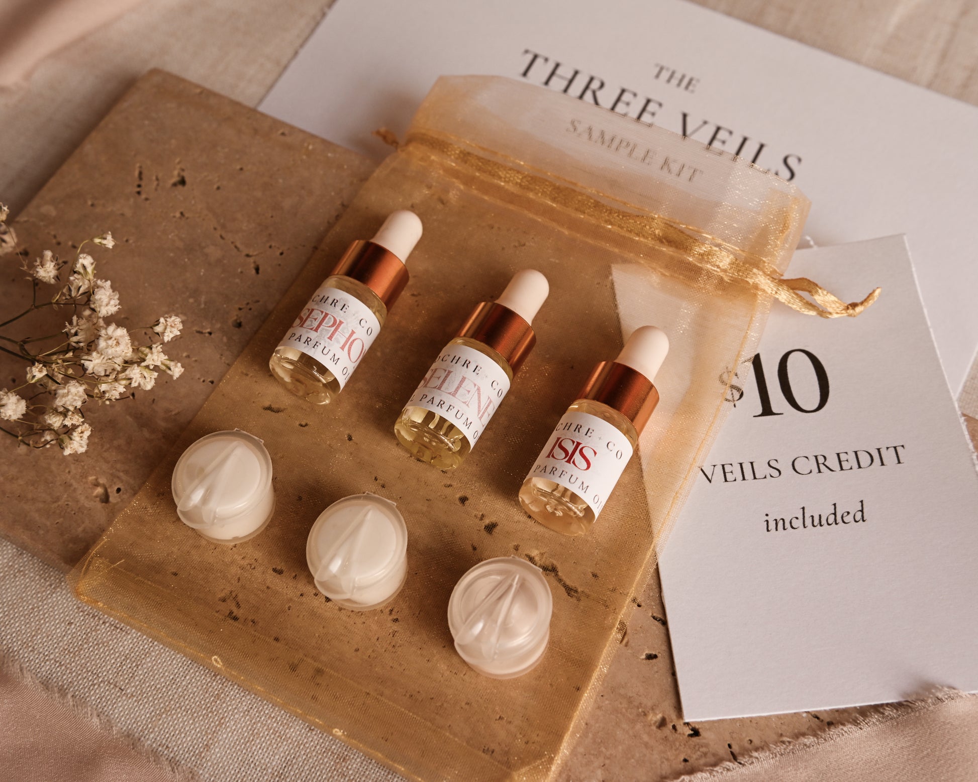 Three small bottles with droppers on a gold chiffon bag labeled 'The Three Veils Sample Kit'.