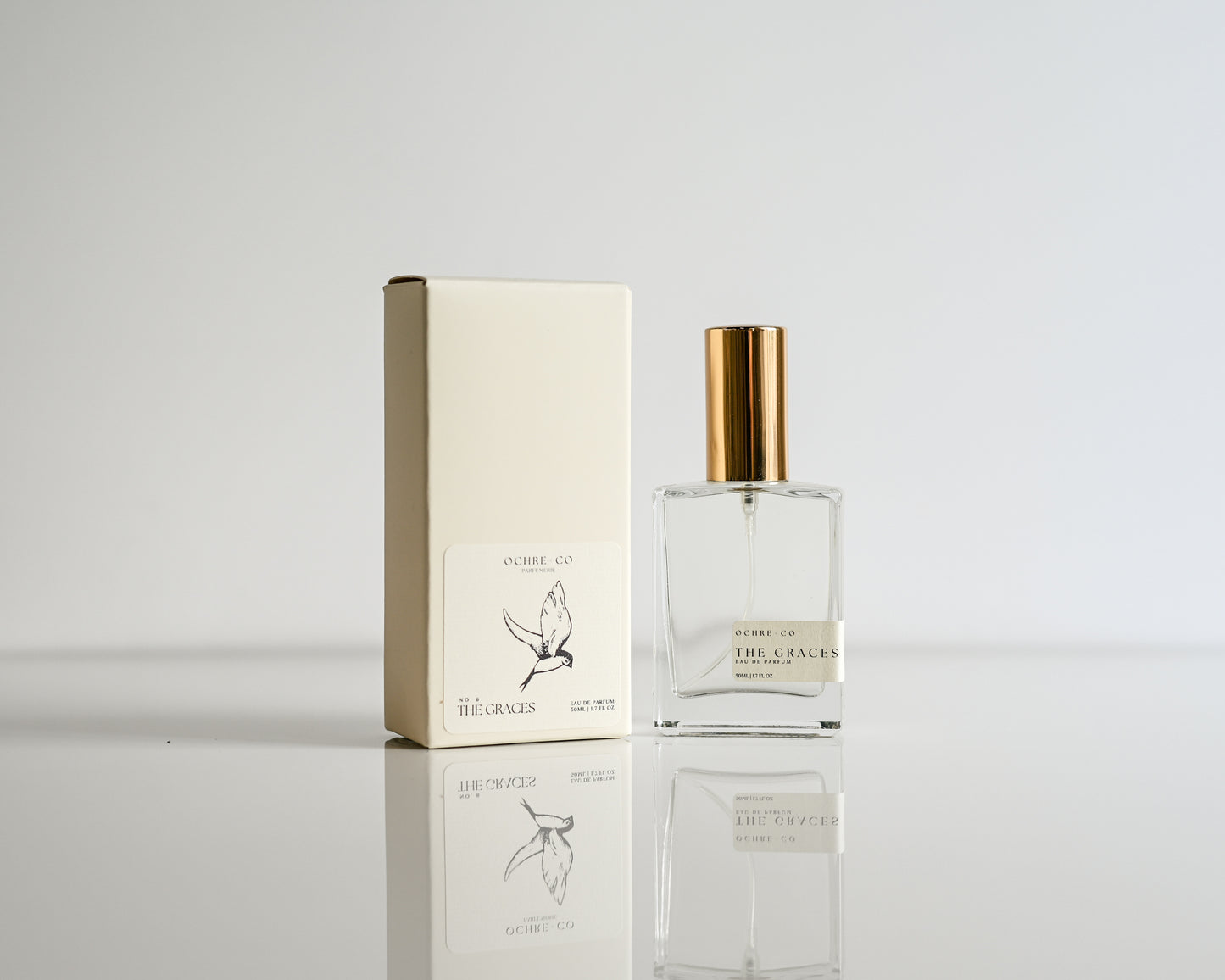 Perfume bottle of The Graces on a white reflective surface and white background