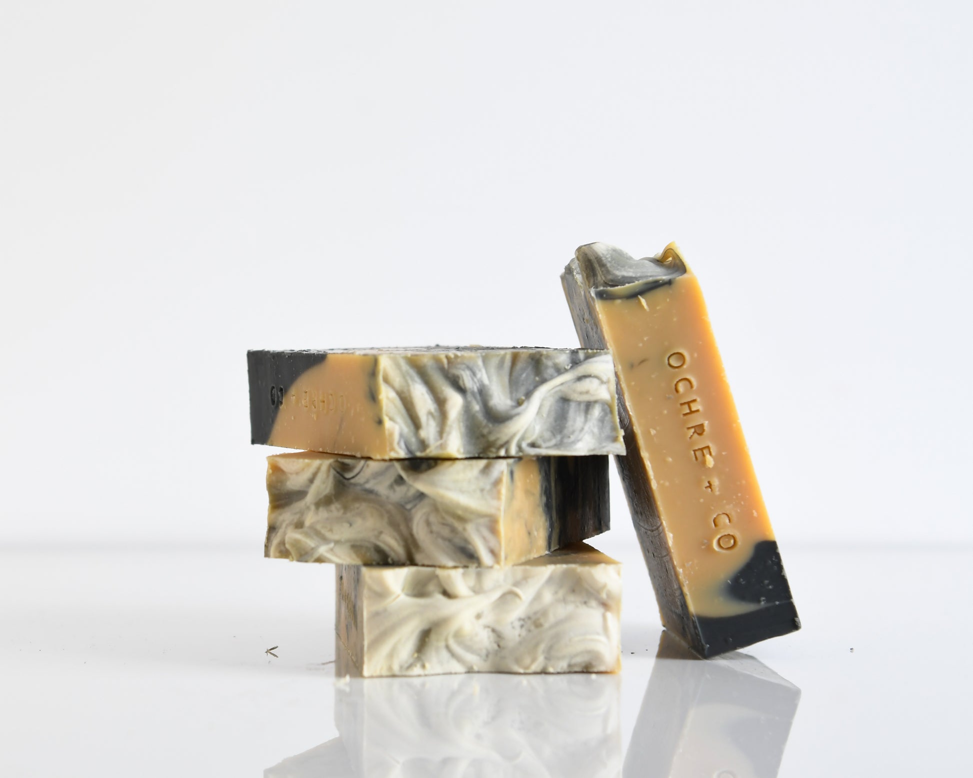 Three bars of soap with marbled patterns stacked on a white background with one bar of soap leaning on the side