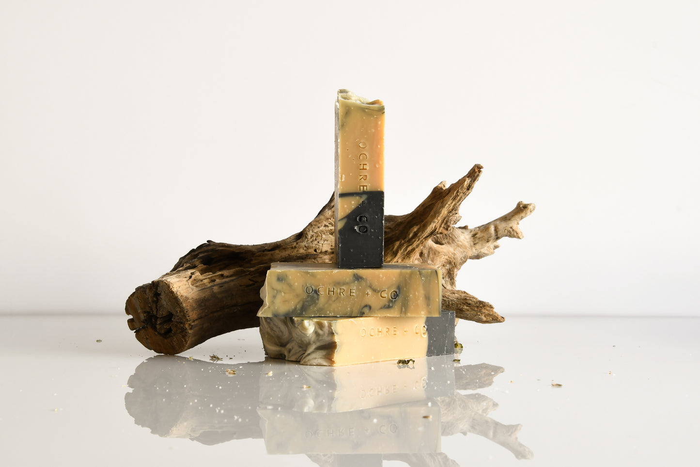 Three bars of soap on a reflective surface with a piece of driftwood in the background